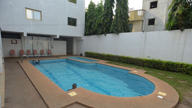 A rectangular swimming pool with a curved edge, surrounded by a low wall and a grassy area. - Jess Hotel (Lomé)