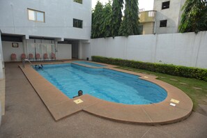 A rectangular swimming pool with a curved edge, surrounded by a low wall and a grassy area.