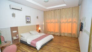 A hotel room with a bed, bedside table, lamp, and a wall-mounted phone. - Jess Hotel (Lomé)