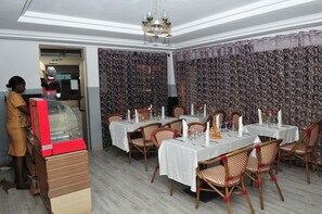 Un restaurant avec des tables dressées, un espace d’accueil et une personne debout derrière un comptoir.