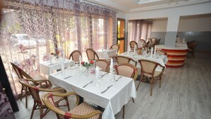 A restaurant with multiple tables set for dining, wicker chairs, and a view of the outdoors. - Jess Hotel (Lomé)