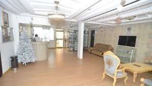 A spacious living area with a wooden floor, a reception desk, a Christmas tree, a sofa, a TV, and a glass cabinet. - Jess Hotel (Lomé)