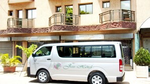 A white van parked in front of a building with balconies and windows. - Jess Hotel (Lomé)
