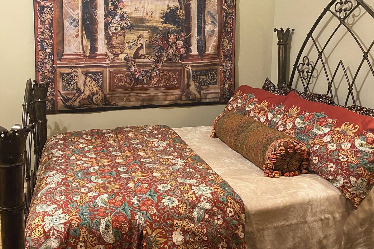 A bedroom with a large tapestry, a bed with floral bedding, and a metal headboard.