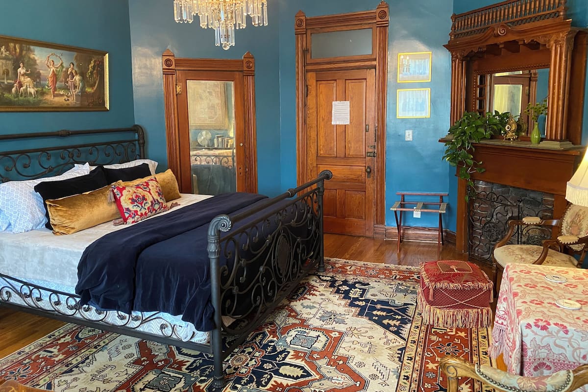 A bedroom with a bed, a chandelier, a wooden door, a mirror, and a fireplace.