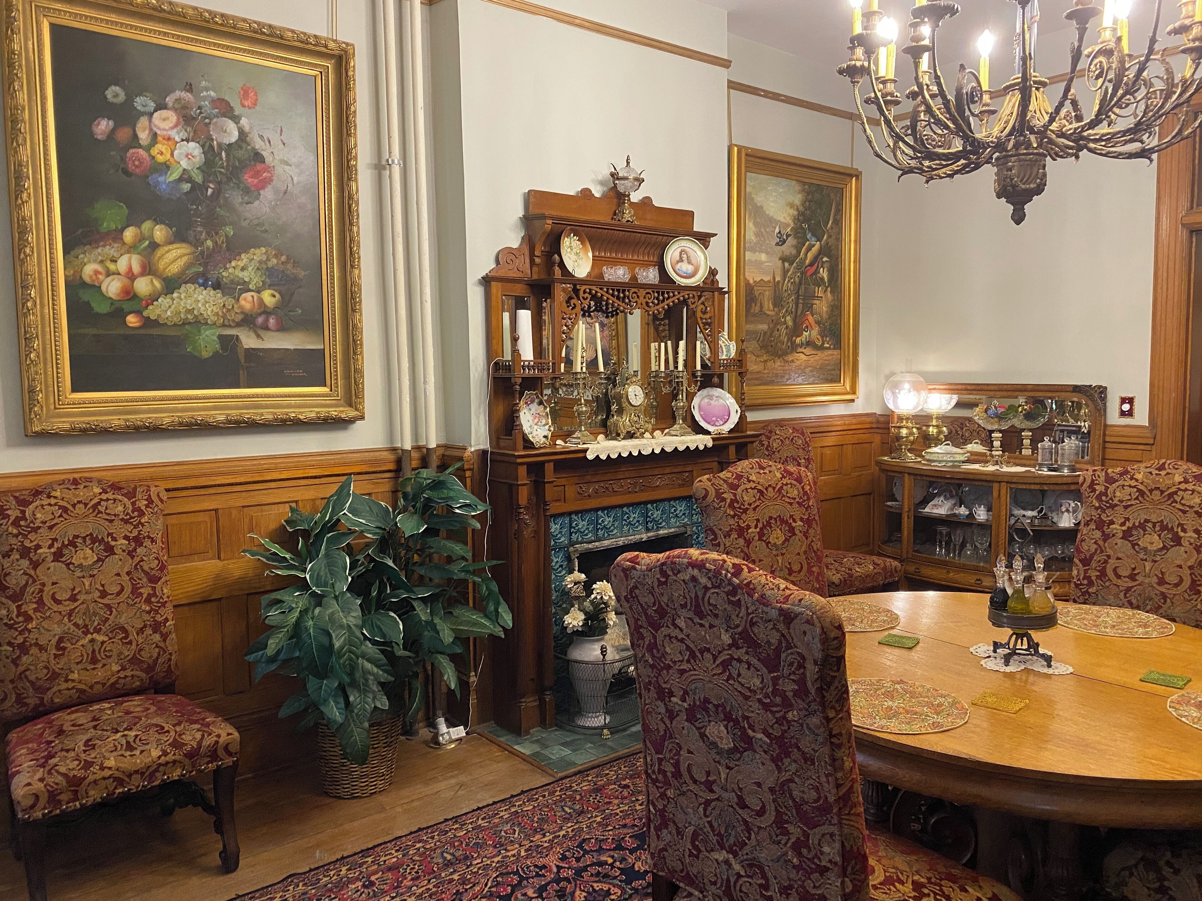 Une salle à manger traditionnelle, agrémentée de meubles richement décorés, d’un lustre et d’un grand tableau représentant des fleurs.