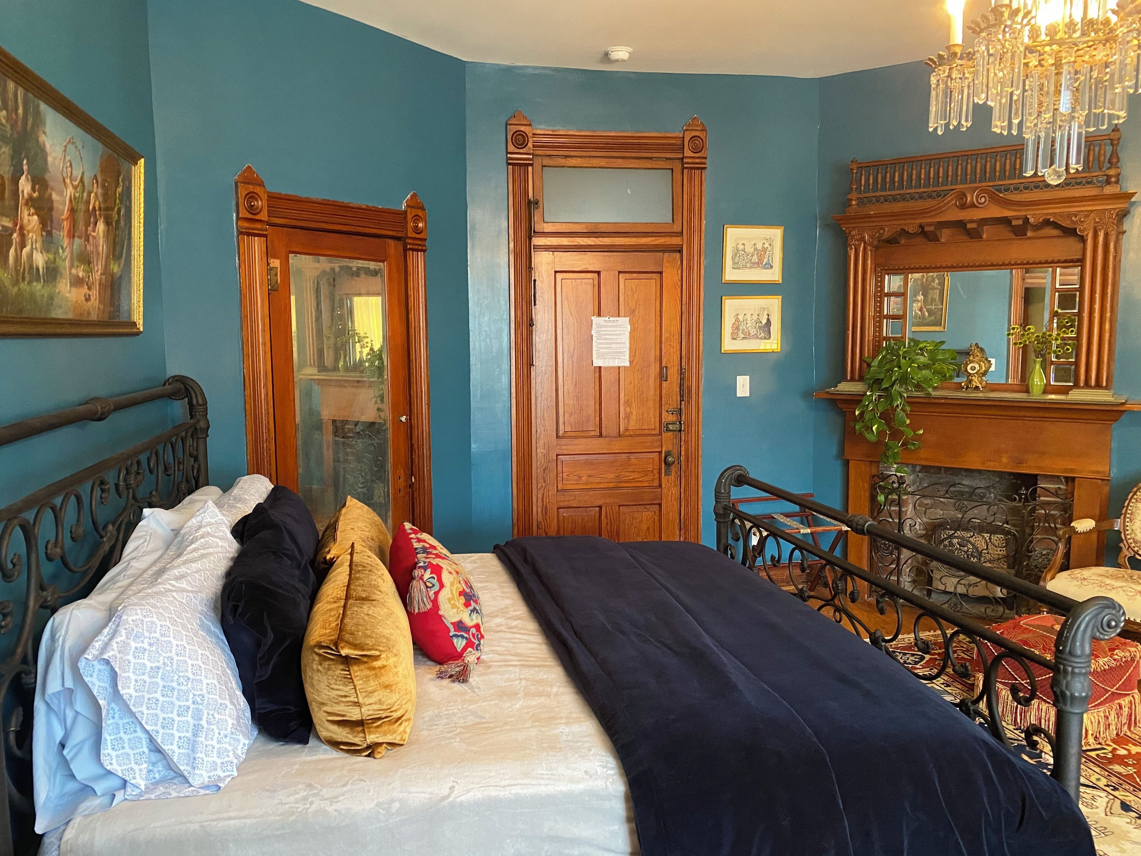 A bedroom with a bed, wooden doors, a fireplace, and a chandelier.