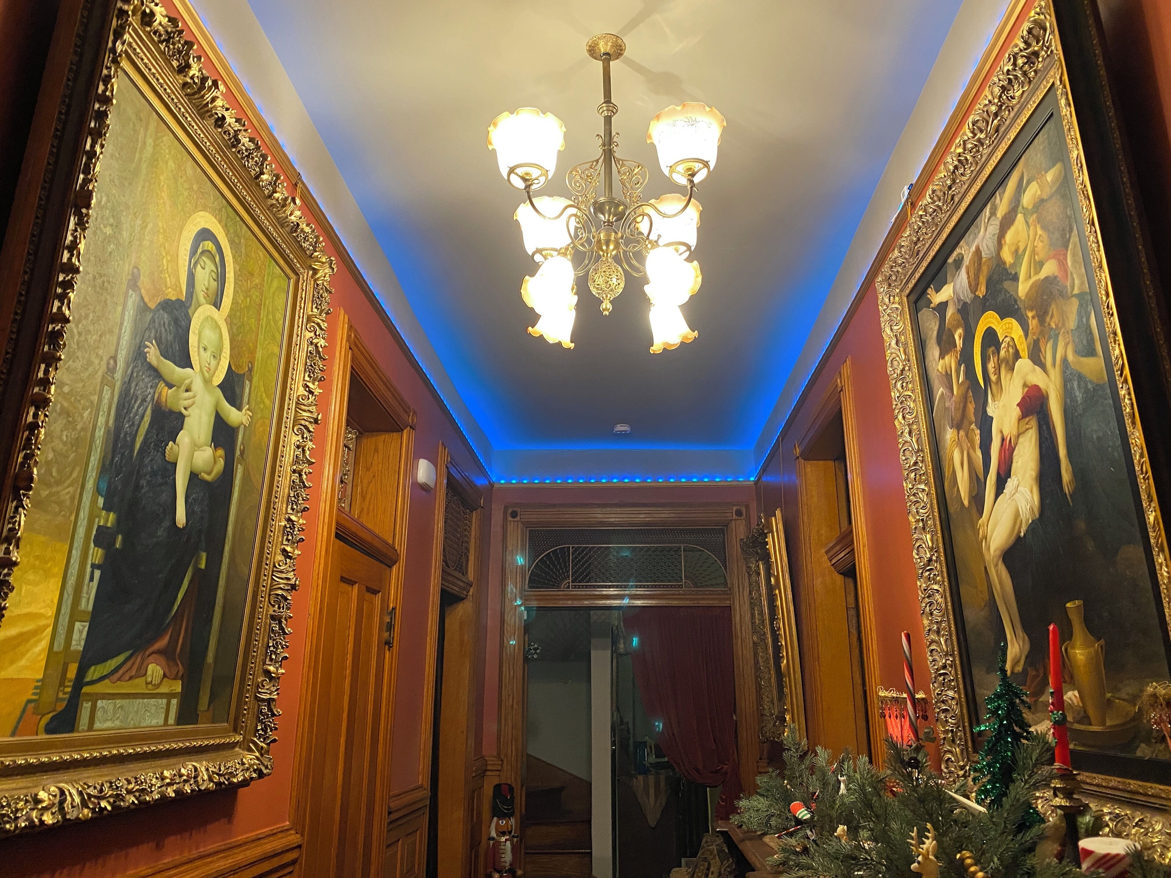 A hallway with ornate paintings, a chandelier, and Christmas decorations.