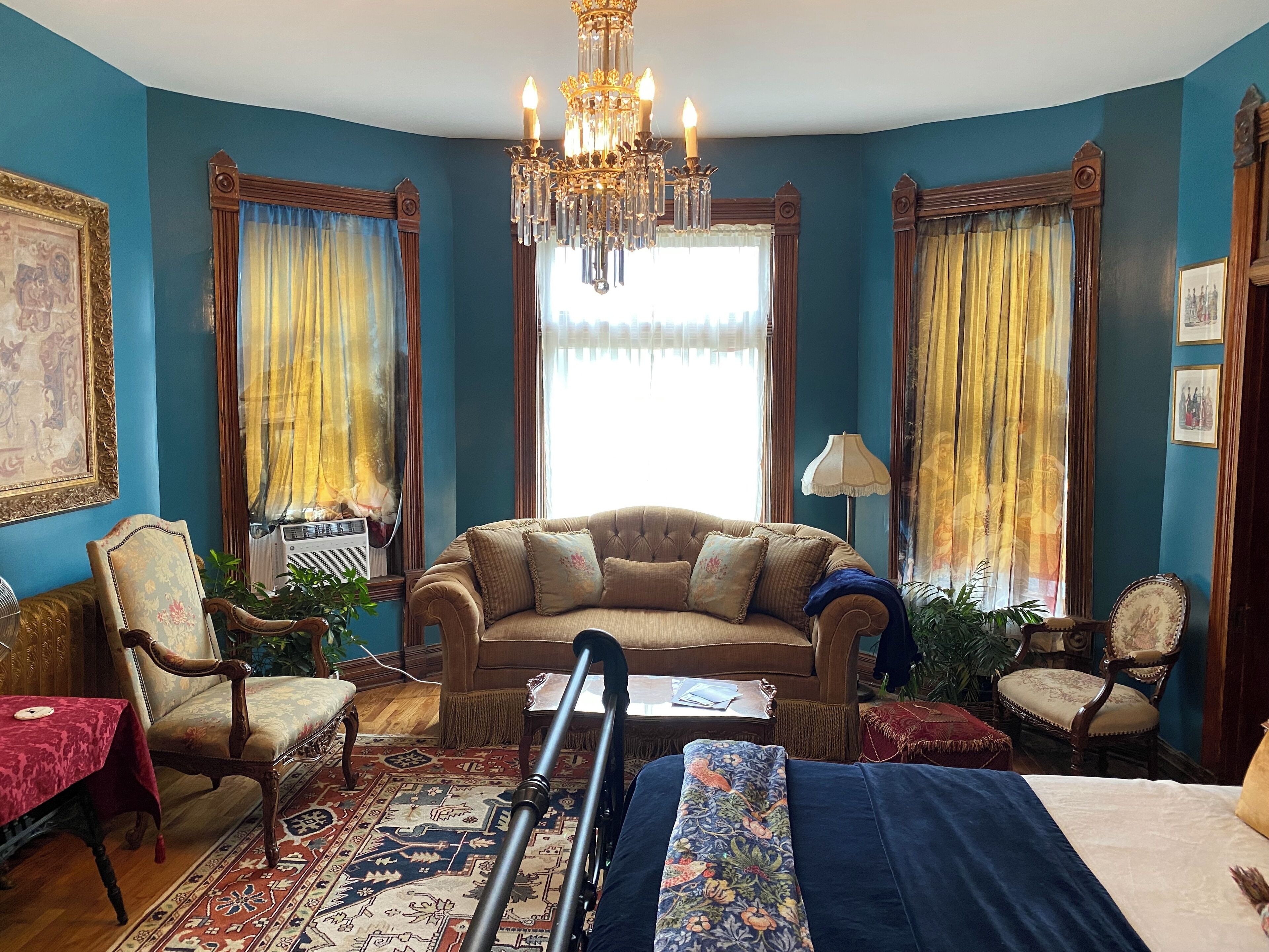 A room with a large sofa, two armchairs, a chandelier, and a large window with curtains.
