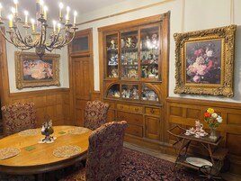 A dining area with a wooden table, ornate chairs, a chandelier, and a cabinet with glass doors.