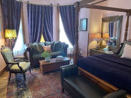 A bedroom with a four-poster bed, a sofa, a chair, and a small table with a plant.