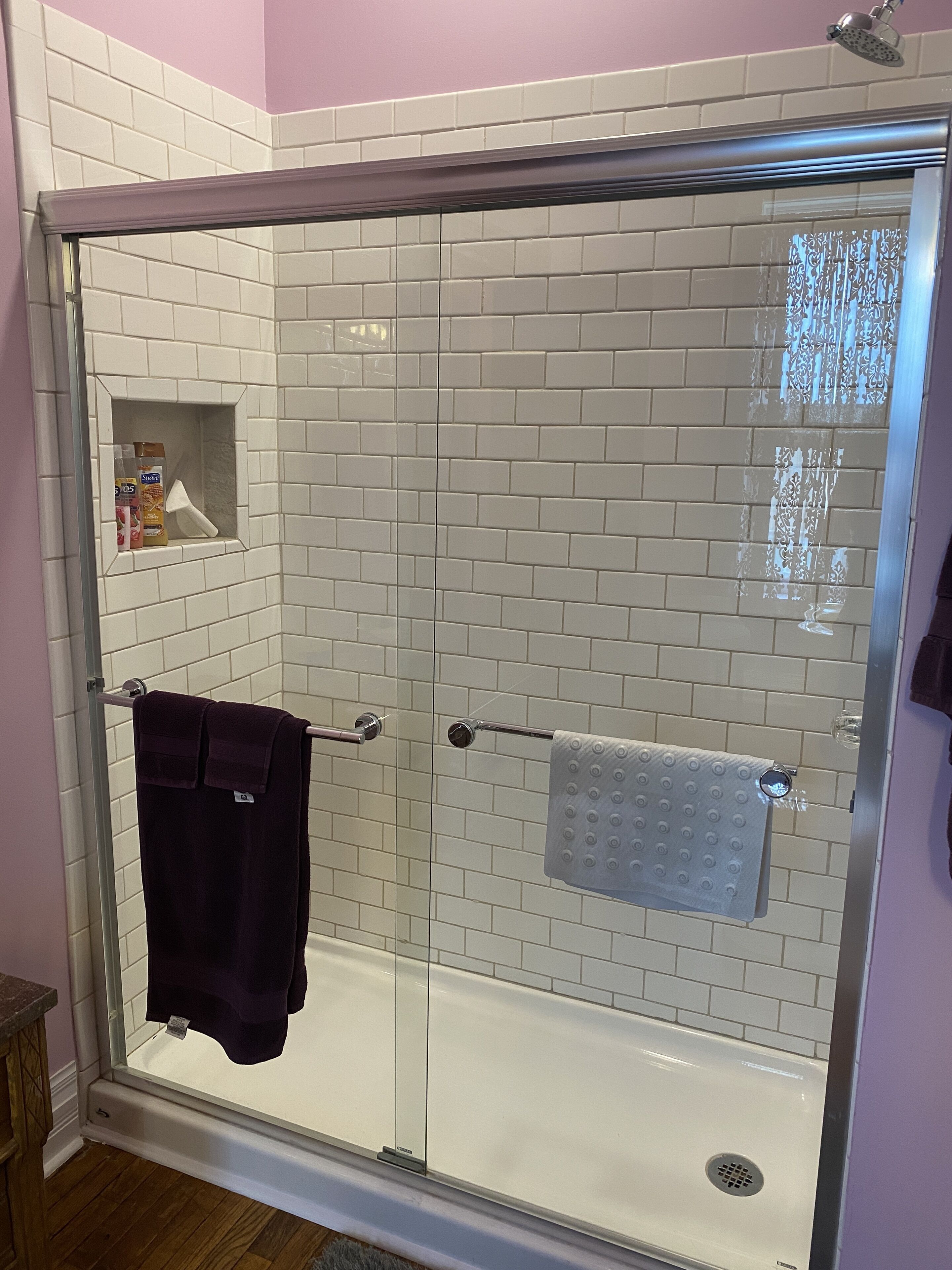 A glass-enclosed shower with white subway tiles and a glass door.