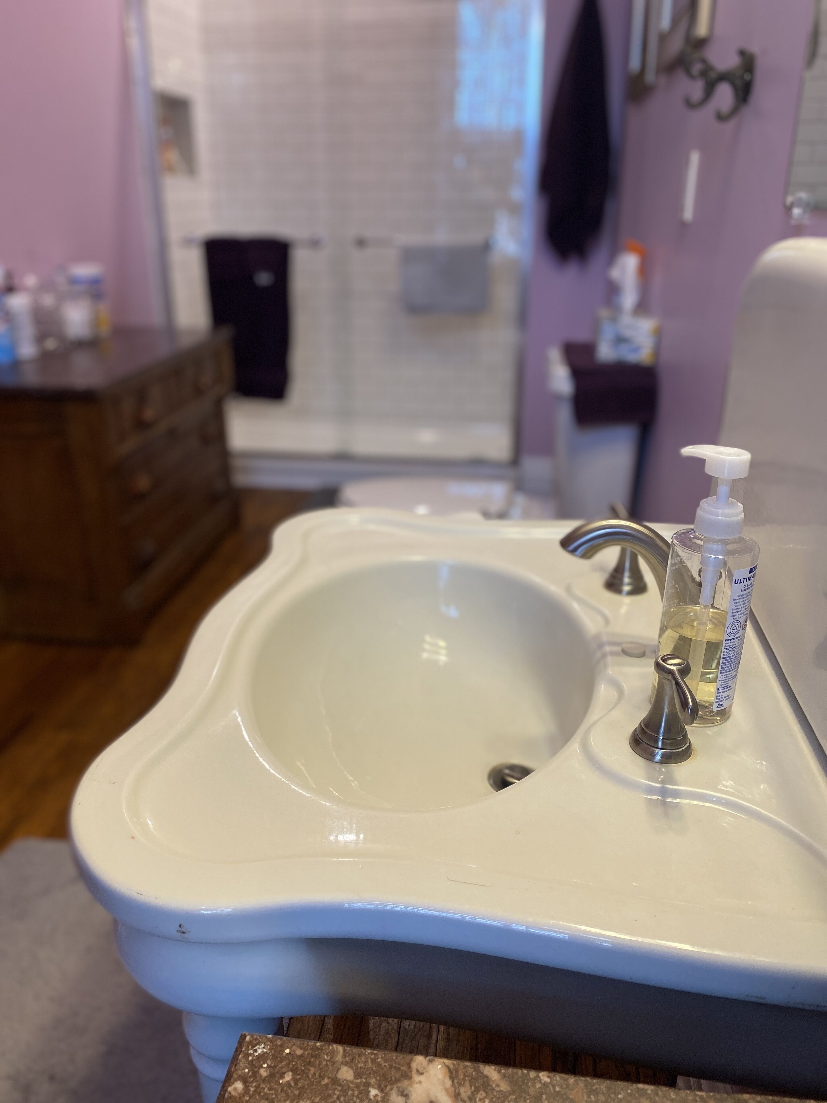Un baño con un lavamanos blanco, un cabezal de ducha de mano y una botella de jabón para las manos.