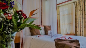 A neatly made bed with white linens, a brown decorative pillow, and a vase of flowers on the side.