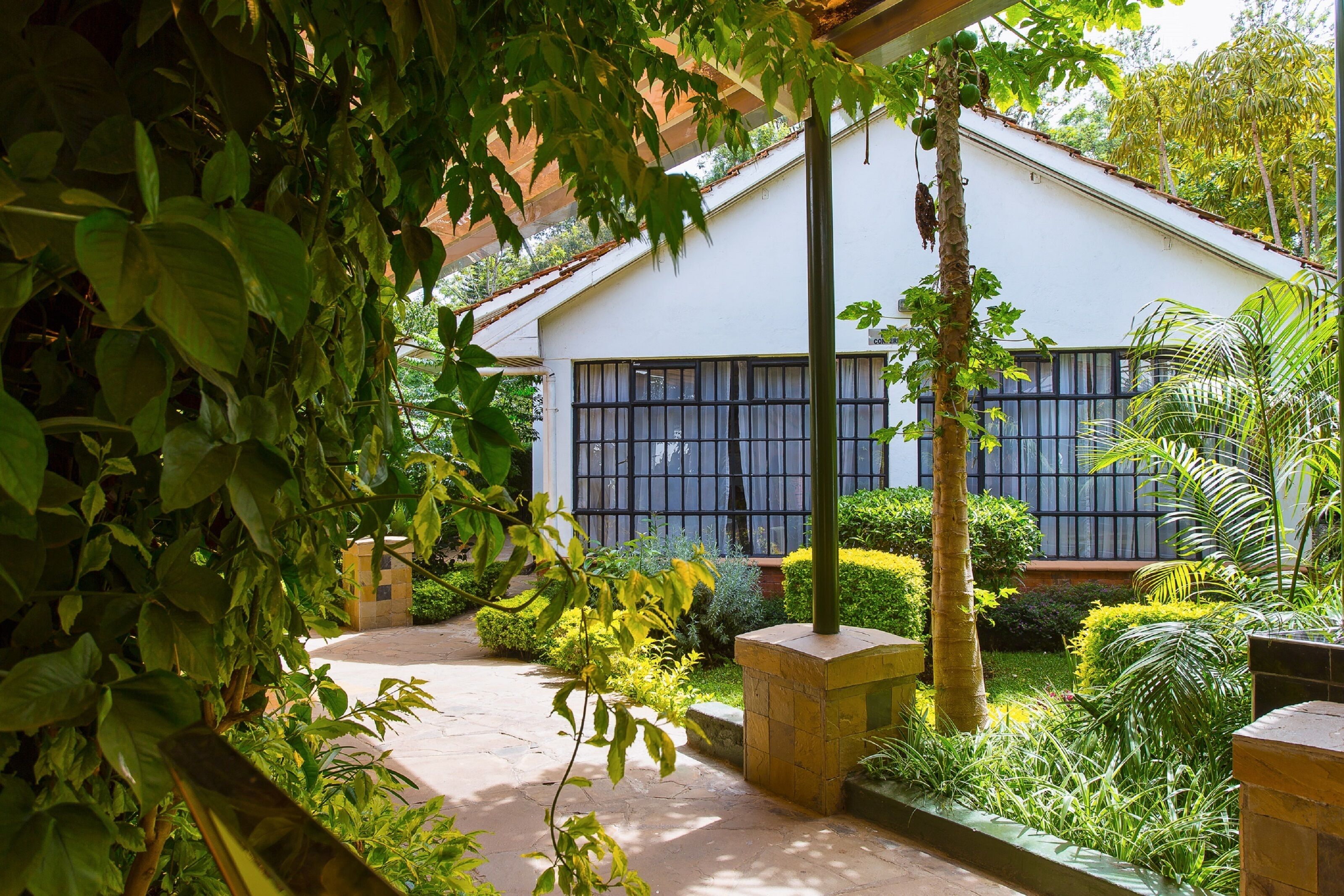 Un bâtiment doté de grandes fenêtres et d’un jardin où poussent différentes espèces de plantes, ainsi qu’un sentier.