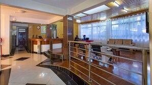 A hotel lobby with a reception desk, seating area, and a staircase.