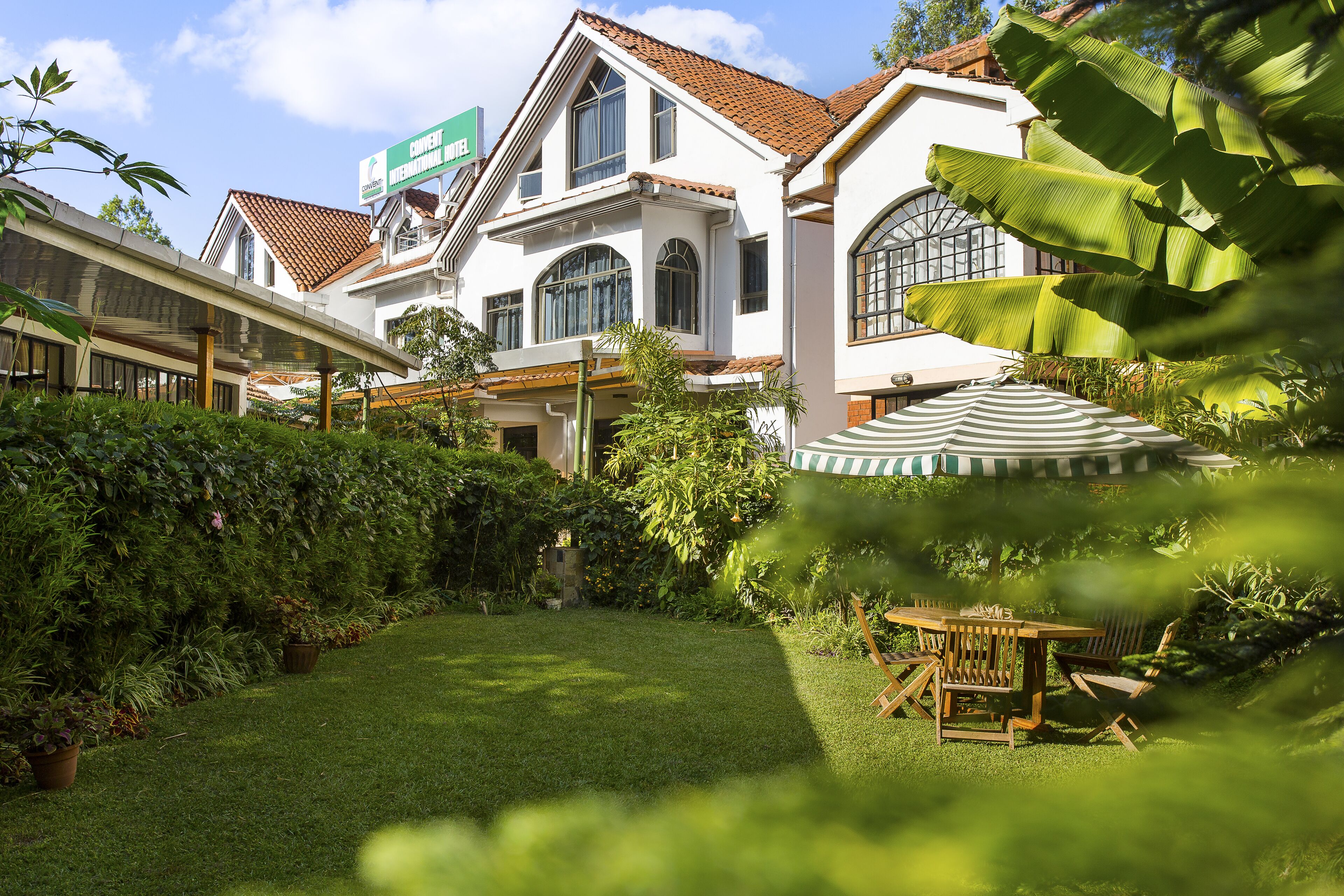 A hotel with a well-maintained garden, a covered outdoor seating area, and a sign indicating it is a conference hotel.