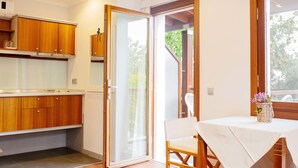 Una cocina con armarios de madera, encimera blanca y puerta corrediza de vidrio que da a un área exterior.