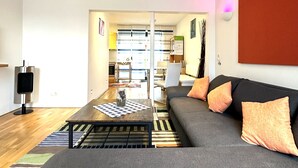 A modern living room with a grey sofa, orange cushions, a coffee table, and a TV. - Schacht85 (Oberhausen)
