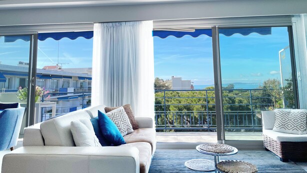 Un salon moderne avec un canapé, une petite table ronde et une vue sur la mer grâce à de grandes fenêtres.