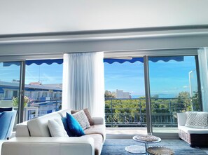 A modern living room with a sofa, a small round table, and a view of the sea through large windows.