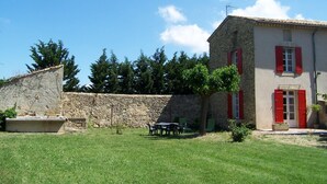 A stone building with red shutters, a stone wall, and a grassy yard with a table and chairs. - Apartment in a Provencal farmhouse in the Orange countryside (Orange)
