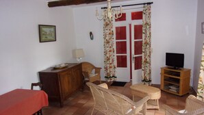 A room with a dining table, wicker chairs, a television on a wooden stand, and a door with red shutters. - Apartment in a Provencal farmhouse in the Orange countryside (Orange)