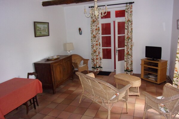 A room with a dining table, wicker chairs, a television on a wooden stand, and a door with red shutters. - Apartment in a Provençal farmhouse in the countryside near Orange (Orange)