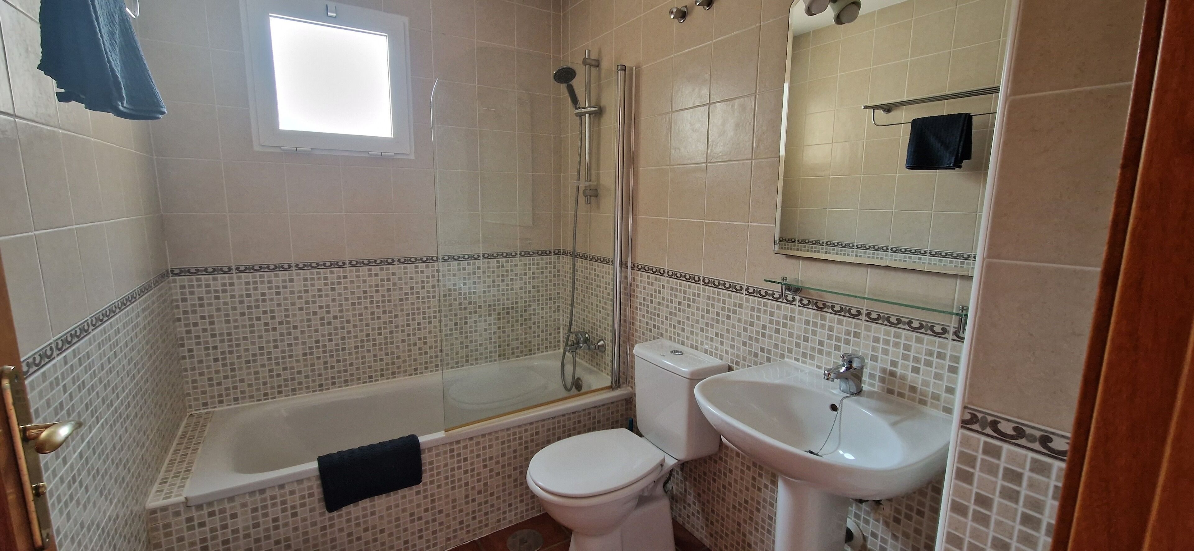 A bathroom with a bathtub, toilet, and sink, all with tiled walls and a patterned border.