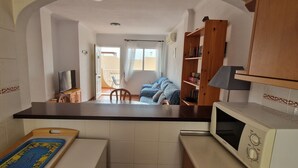 Une cuisine compacte équipée d’un micro-ondes, d’une petite table et d’un téléviseur. On aperçoit un balcon à travers une porte ouverte.