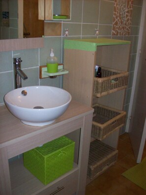 Un baño con lavamanos blanco, dispensador de jabón verde y cestas de mimbre.