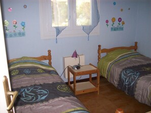 Una habitación con dos camas de madera, una mesita y una ventana.