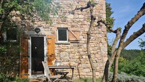 A rustic stone building with a wooden door, a small window, and a table with chairs outside. - NEST OF LOVE in South Ardèche (Les Vans)