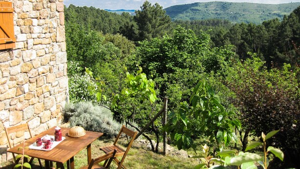 A stone building with a table and chairs set outdoors, overlooking a vineyard and hills. - NEST OF LOVE in South Ardèche (Les Vans)