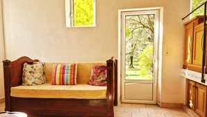 A room with a wooden sofa, a small table, a door leading outside, and a window with a view of trees. - NEST OF LOVE in South Ardèche (Les Vans)