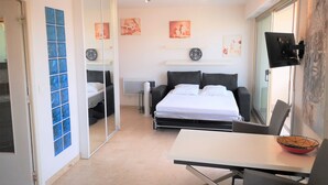 Un dormitorio moderno con cama, mesitas de noche, un escritorio y una silla. Se observan relojes de pared y obras de arte.