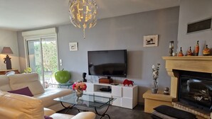 A modern living room with a sofa, a glass coffee table, a flat-screen TV, a fireplace, and decorative items. - Daniela's House in Peace and Comfort (Sarlat-La-Canéda)