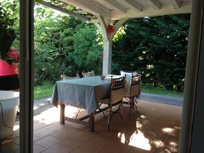 An outdoor patio with a table and chairs, surrounded by a wooden pergola and lush greenery.