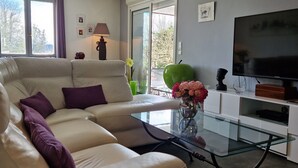 A modern living room with a sectional sofa, a glass coffee table, a flat-screen TV, and a decorative apple. - Daniela's House in Peace and Comfort (Sarlat-La-Canéda)