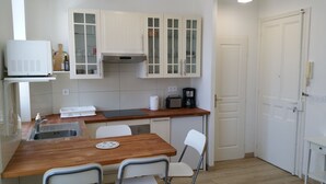 A compact kitchen with white cabinets, a wooden countertop, a sink, a coffee maker, and a dining area with two chairs. - 2 rooms Full City Center, Clim WIFI Absolute Calm at 400 m Promenade des Anglai (Nice)