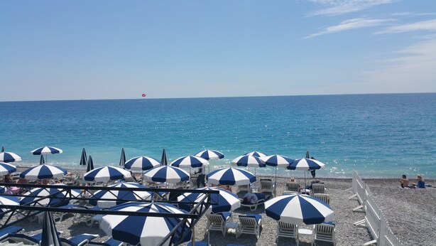 A beach with rows of white and blue striped umbrellas and lounge chairs facing the sea. - 2 rooms Full City Center, Clim WIFI Absolute Calm at 400 m Promenade des Anglai (Nice)