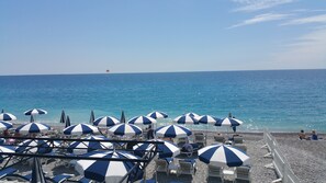 A beach with rows of white and blue striped umbrellas and lounge chairs facing the sea.