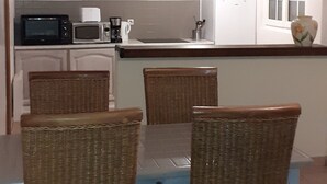 A dining area with wicker chairs and a table, a kitchen with a microwave and toaster, and a window with blinds.