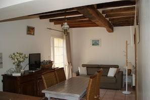 A dining area with a wooden table and chairs, a television on a cabinet, and a sofa in the background. - Charming Normandy cottage chestnut 15 km from Etretat in Upper Normandy (Bretteville-Du-Grand-Caux)