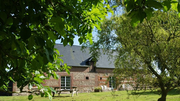 A stone building with a sloped roof, surrounded by a grassy area with a picnic table and chairs.