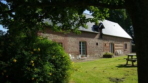 A rustic stone building with a sloped roof, a grassy yard, and a picnic table.