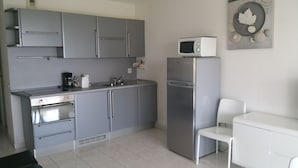 A compact kitchen with grey cabinets, a stainless steel refrigerator, a microwave, a sink, and a small white table.