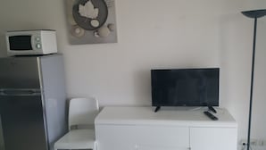A kitchenette with a microwave, refrigerator, and a flat-screen TV on a white cabinet.