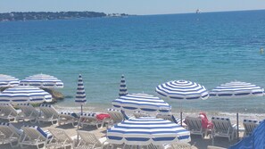 Una playa con filas de tumbonas y sombrillas a rayas, una vista despejada del mar y un barco a lo lejos.