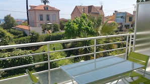 A balcony with a glass table and chairs, overlooking a residential area with houses and greenery.